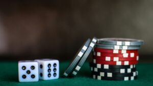 Two dice and stacks of red, black, and silver casino chips on a green surface