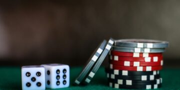 Two dice and stacks of red, black, and silver casino chips on a green surface