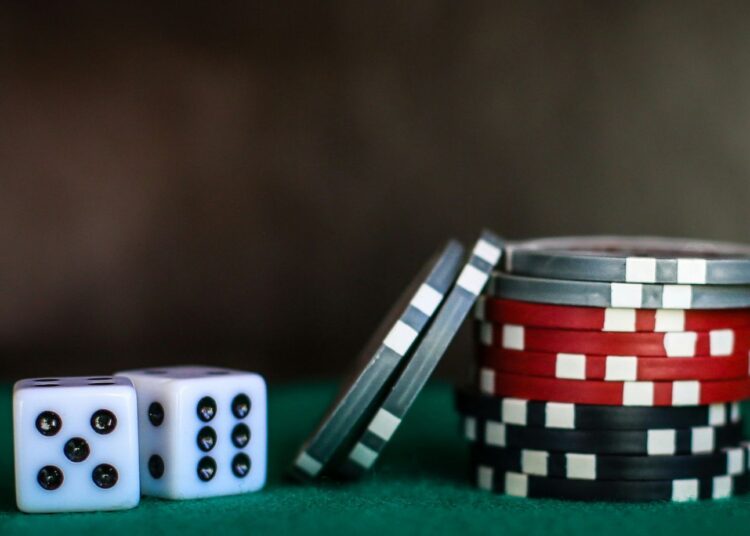 Two dice and stacks of red, black, and silver casino chips on a green surface